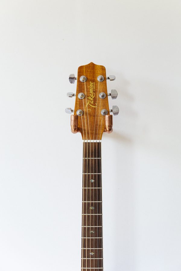 beyaz duvar üzerine monte edilmiş bakır gitar askısı üzerinde ahşap tonlarında asılı gitar ön görünüş