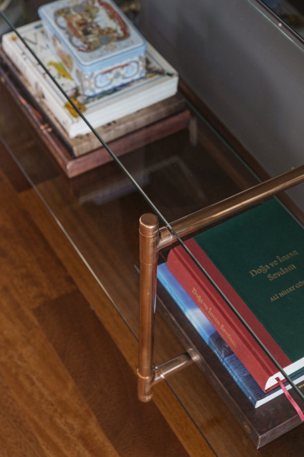 gri duvar önünde bakır detaylı raflarında kitaplar bulunan 2 katlı cam TV Ünitesi üst görünüş