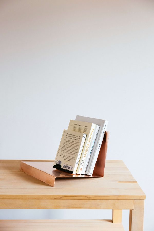 huş masa üzerinde duran mat bakır kitap standı ve 4 adet beyaz renkli kitap iç mekan kullanım