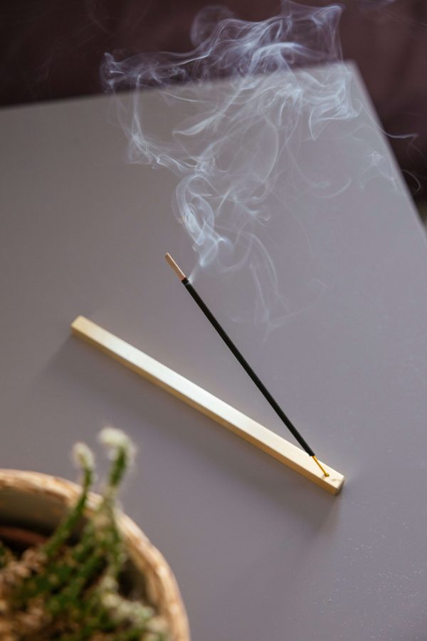 gri masa üzerinde yanan bir tütsünün durduğu pirinç çubuk tütsülük